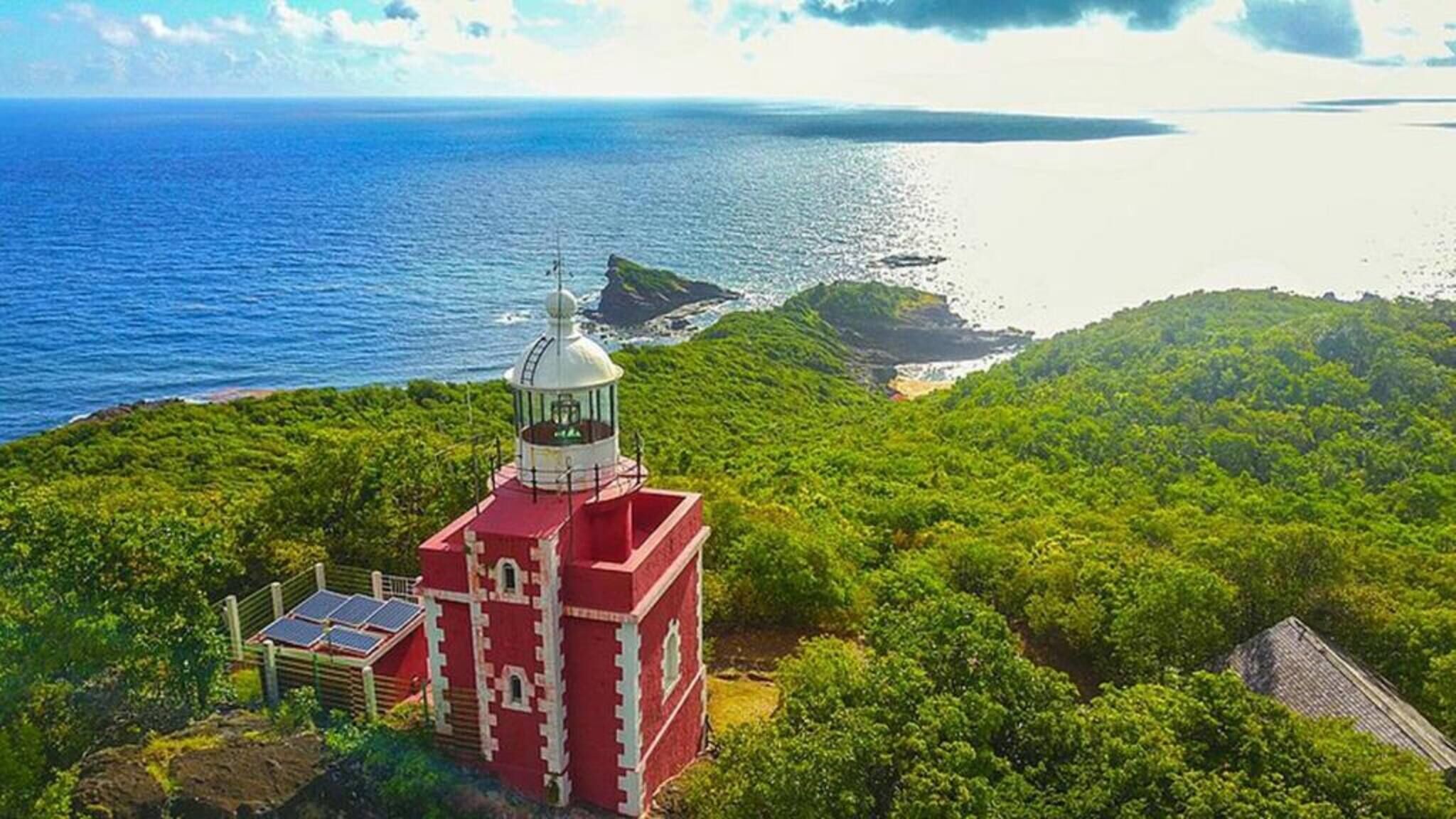 A lighthouse on a lush green hill overlooking a calm sea.