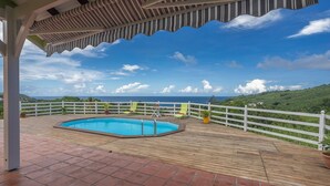 Une terrasse en bois avec une piscine, des rampes blanches et une vue sur l’océan.