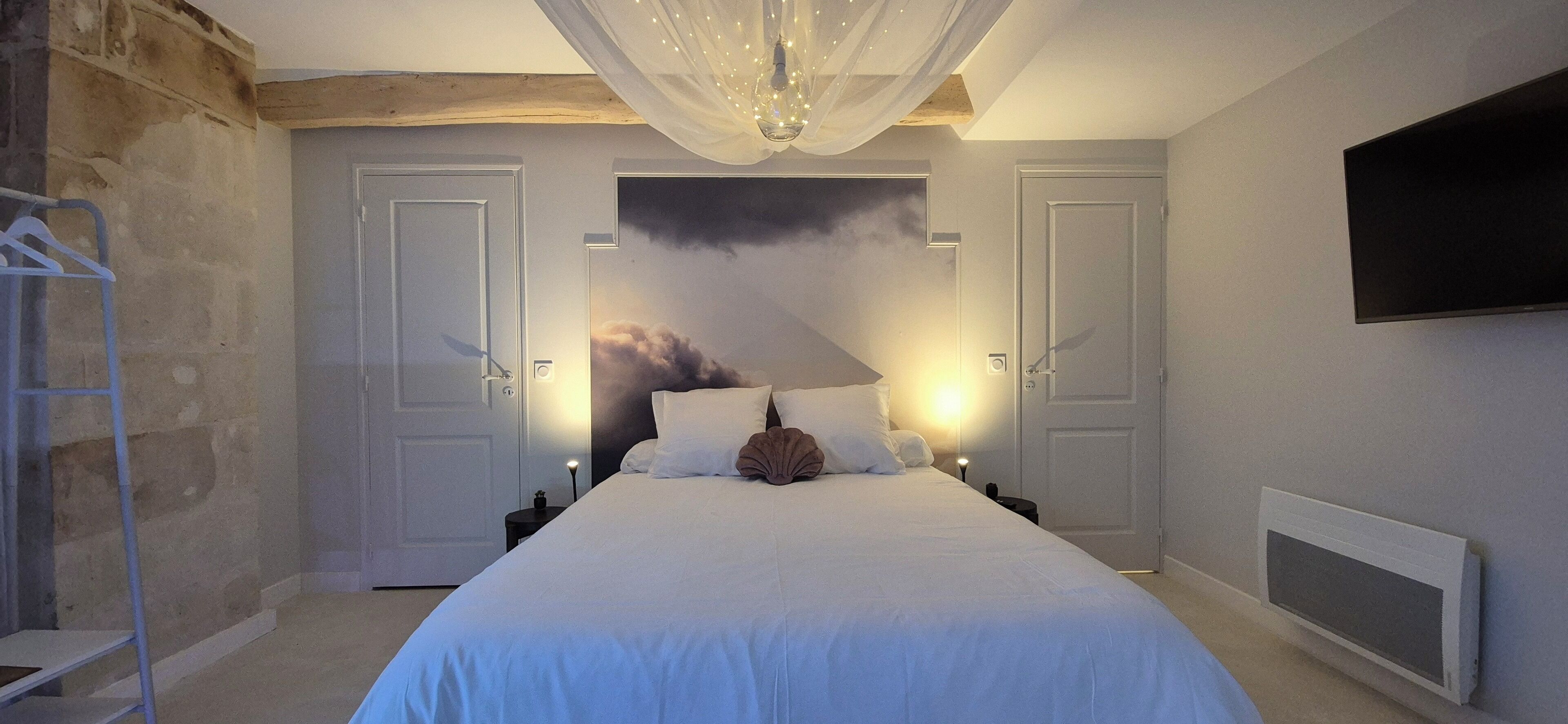 Een slaapkamer met een groot bed, twee nachtkastjes, een aan de muur bevestigde televisie en een plafondlamp.