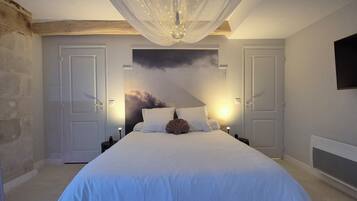 Een slaapkamer met een groot bed, twee nachtkastjes, een aan de muur bevestigde televisie en een plafondlamp.
