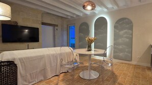 A modern kitchen with a round dining table, clear chairs, a TV mounted on the wall, and a microwave on the counter. - Comfortable cocoon 400m from Saumur cellars, close to golf course, IFCE, Loire... (Saumur)