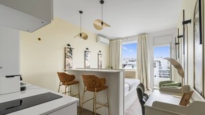Una habitación de hotel moderna con kitchenette, una cama, un escritorio con silla y vista a la ciudad.