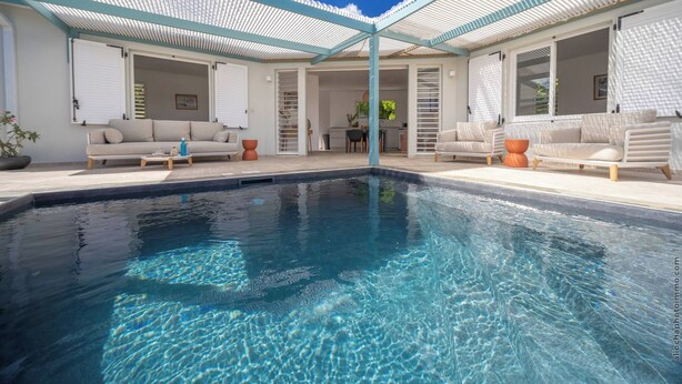 A swimming pool with a covered patio area, outdoor seating, and a kitchen visible through the open doors. - 2 Villas with 2 Swimming Pools (Sainte-Luce)