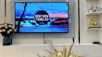 Ein modernes Wohnzimmer mit einem flachbildfernseher an einer weißen Wand, einer dekorativen Uhr und einer Vase mit Trockenblumen auf einem blauen Tisch.