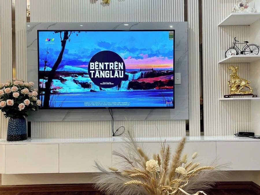 Ein modernes Wohnzimmer mit einem flachbildfernseher an einer weißen Wand, einer dekorativen Uhr und einer Vase mit Trockenblumen auf einem blauen Tisch.
