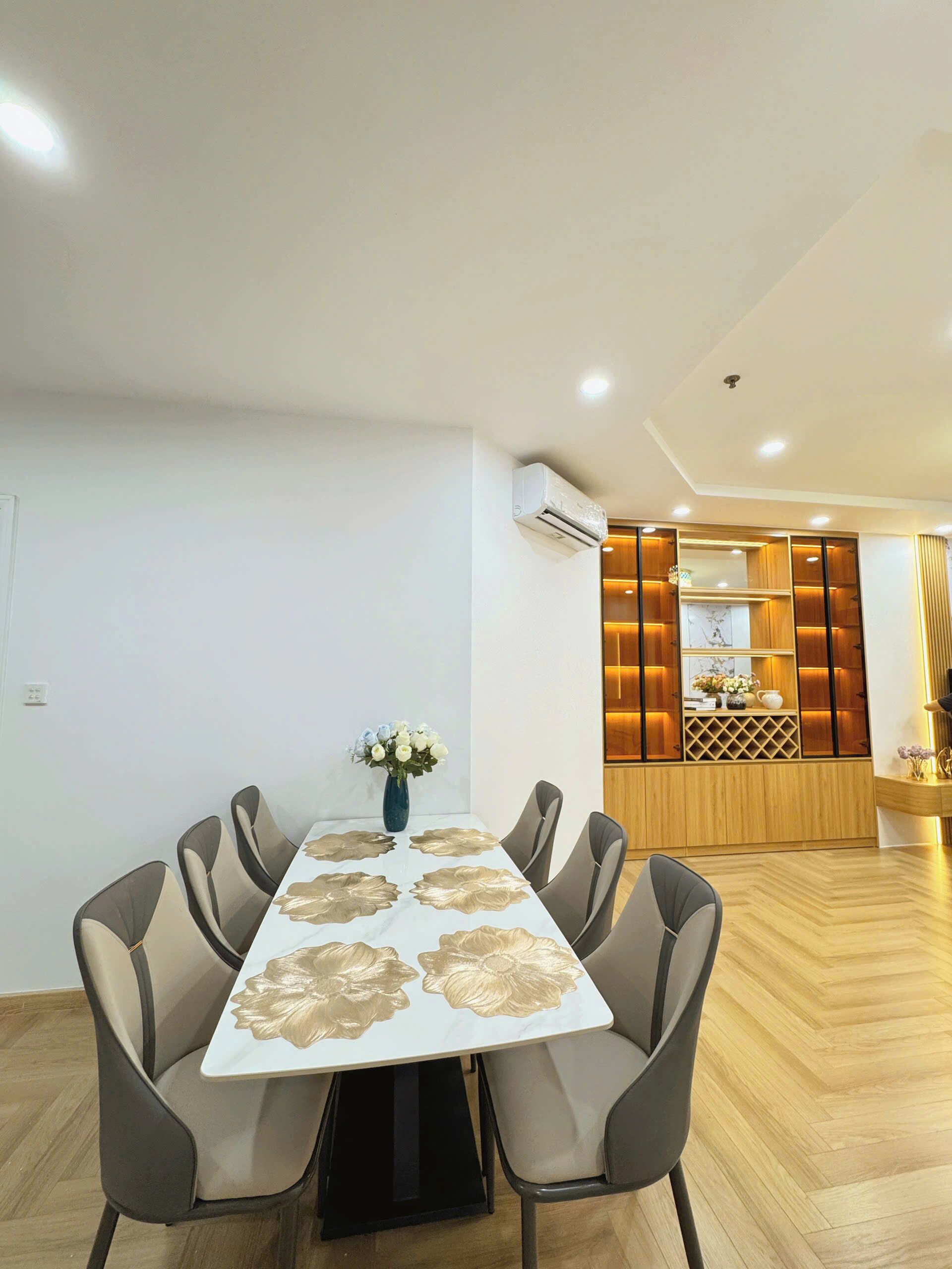 A modern dining area with a white table featuring gold floral patterns, surrounded by six grey chairs.