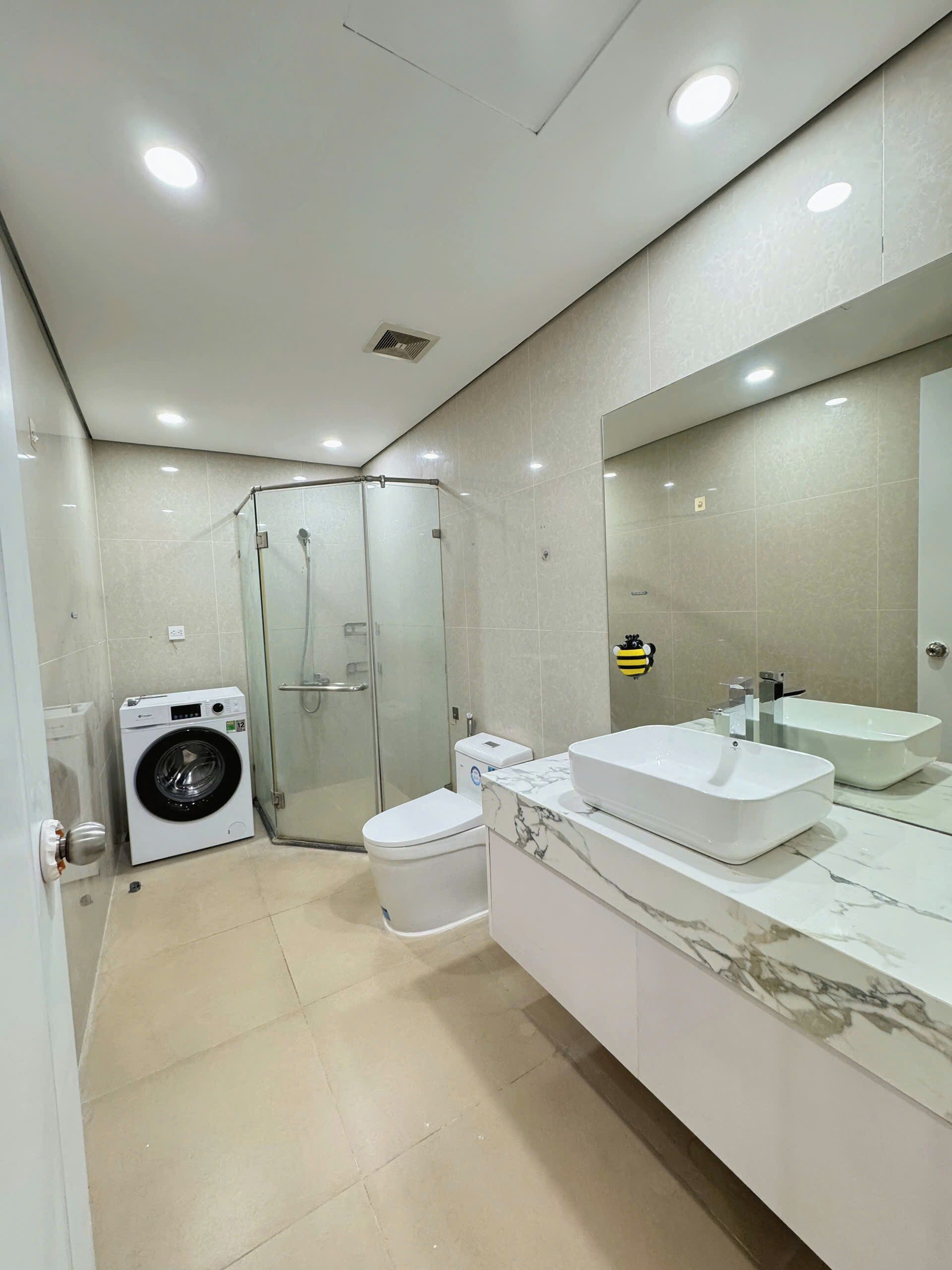Ein modernes Badezimmer mit einer Glaskabine zur Dusche, einer Waschmaschine und einem Waschtisch mit großem Spiegel.
