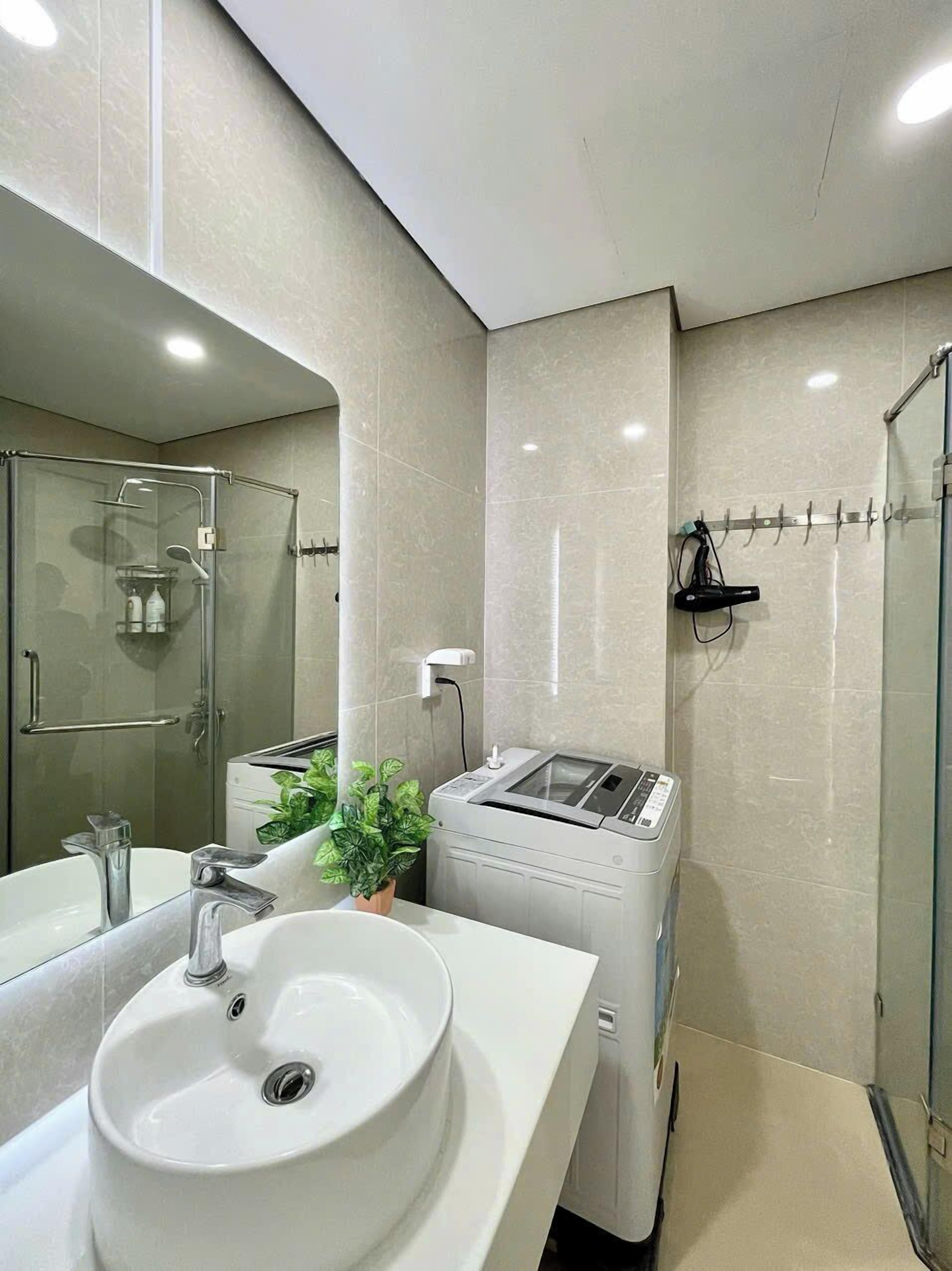 A modern bathroom with a glass-enclosed shower, a white sink, and a compact, wall-mounted washing machine.