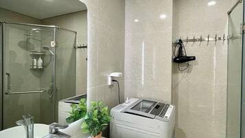 A modern bathroom with a glass-enclosed shower, a white sink, and a compact, wall-mounted washing machine.