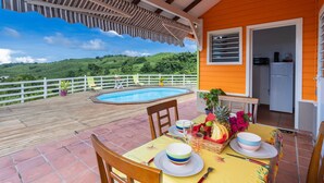 Un espace extérieur abrité avec une piscine, une table à manger dressée avec des assiettes, des bols et un panier de fruits.