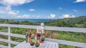 Une table avec des bouteilles et des verres de liqueur Saint James, offrant une vue panoramique sur l’océan et les collines.