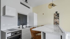 A modern kitchen with white cabinetry, a built-in oven, a sink, and a marble countertop. - Le Botanik: Chic Garden (Fort-de-France)