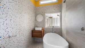 A bathroom with a freestanding bathtub, a wooden vanity, and a round mirror. - Le Botanik: Chic Garden (Fort-de-France)