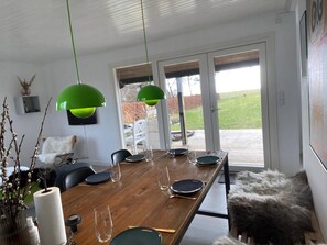 A dining area with a wooden table, chairs, and hanging green pendant lights. - Lovely house with sea view and large terrace (Karrebæksminde)