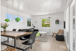 A modern living room with a wooden dining table, black and green chairs, a round white table, and a wicker chair. - Lovely house with sea view and large terrace (Karrebæksminde)