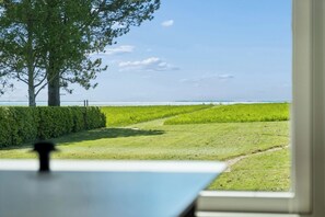 A view from a window overlooking a grassy field with a tree and a distant body of water. - Lovely house with sea view and large terrace (Karrebæksminde)