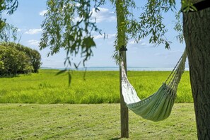 A hammock tied between trees in a grassy field with a view of the sea.