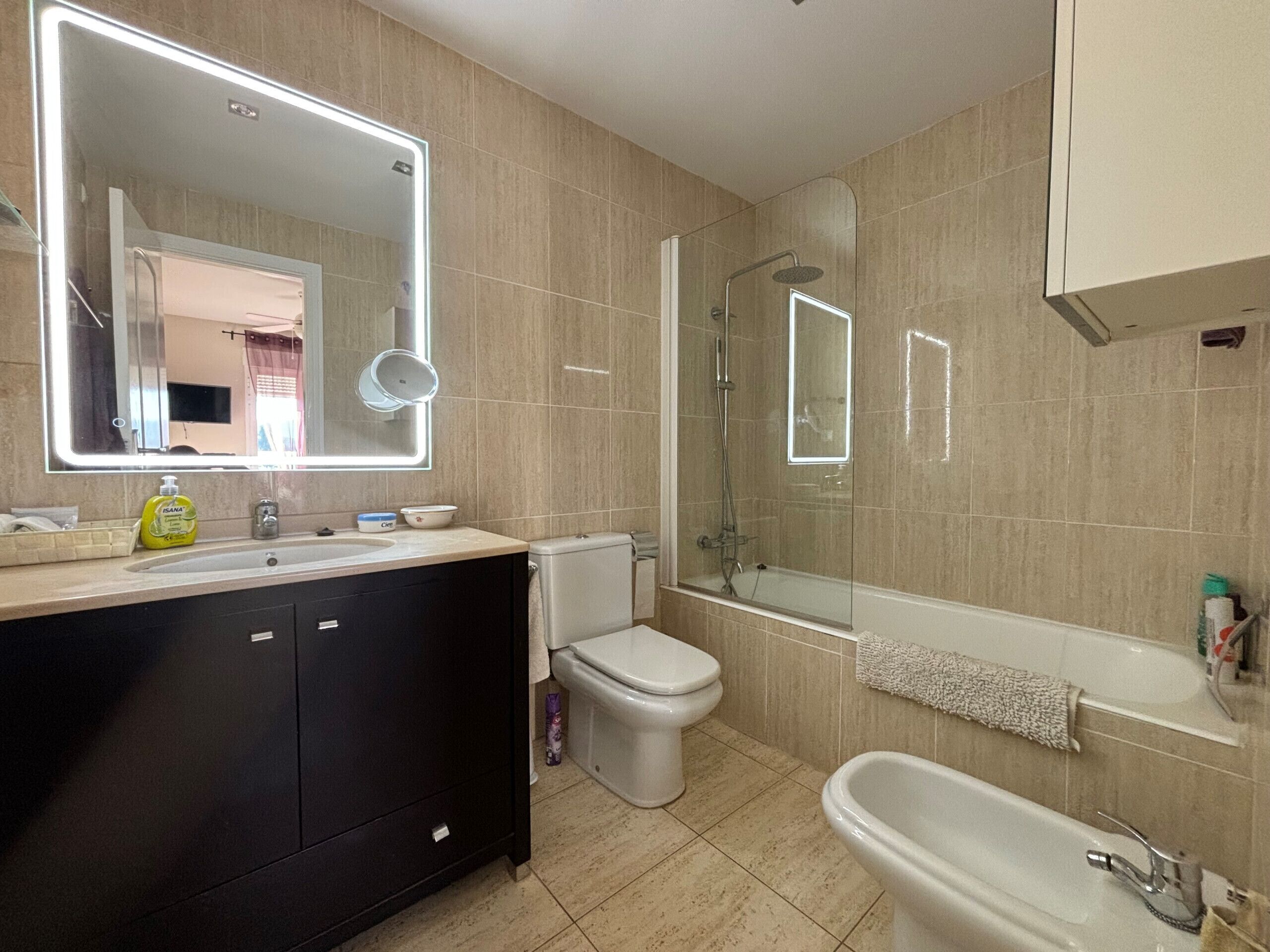 Et moderne badeværelse med et stort spejl, badekar, bruser og toilet.