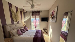A bedroom with a bed, a ceiling fan, a TV, and a large window with curtains. - CLEMENVILLA III (Denia)