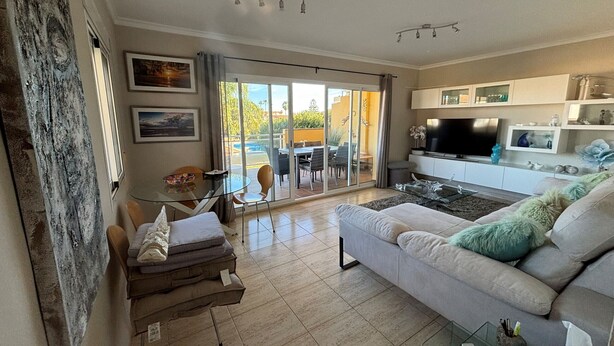 A spacious living room with a sofa, a glass coffee table, and a TV. There is a sliding glass door leading to an outdoor area with a table and chairs. - CLEMENVILLA III (Denia)