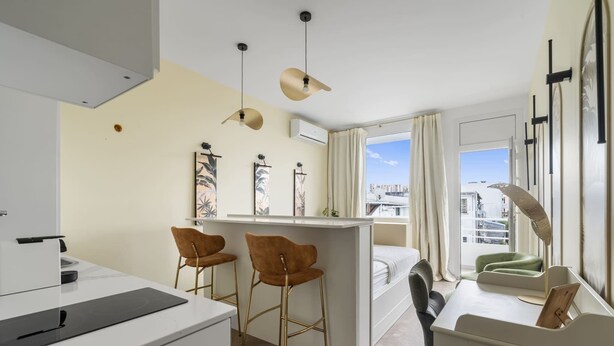 Moderni ja kompakti hotellihuone, jossa on pieni keittiönurkkaus, sänky, työpöytä ja näkymä kaupunkiin.