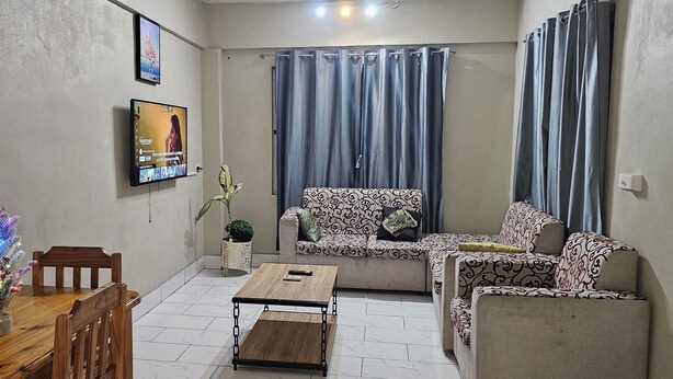 A living room with a sofa, a coffee table, a TV mounted on the wall, and a small decorative plant.