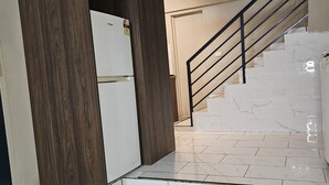 A kitchen with a refrigerator, a wooden cabinet, a staircase with a metal railing, and a tiled floor.