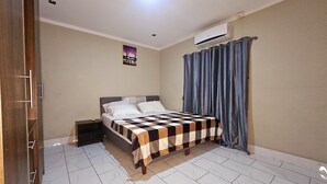 A bedroom with a bed, a nightstand, a wall-mounted air conditioner, and a window with curtains.