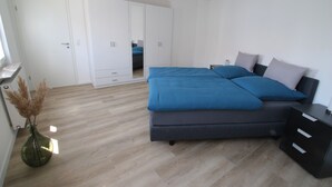 Een slaapkamer met een bed, nachtkastje, dressoir, kledingkast en een vaas met gedroogde planten.