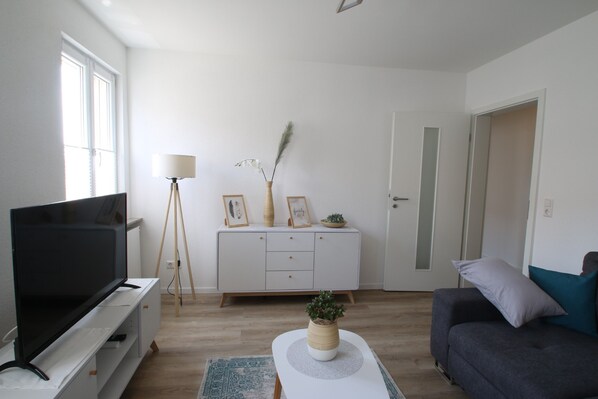 A modern living room with a flat-screen TV, a white console table, a grey sofa, and a floor lamp.