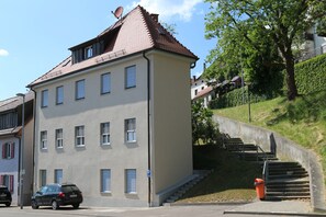 A multi-story building with a sloped roof, a parking area, and a staircase leading to a higher level.