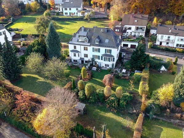 A large, two-story house with a sloped roof, surrounded by a well-maintained lawn and various trees.