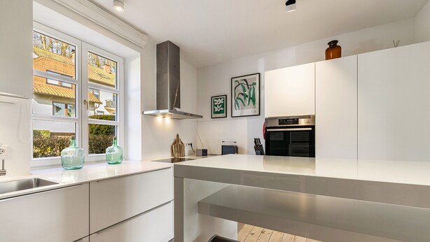 A modern kitchen with white cabinetry, a stainless steel range hood, and a window with a view of buildings. - Apartment 'Erdgeschoss, 65qm' with Wi-Fi (Attendorn)
