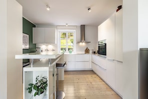 A modern kitchen with white cabinets, a wooden floor, and a window with a view of greenery.