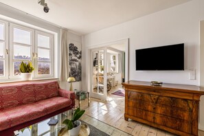A living room with a sofa, a TV, a wooden cabinet, and a view through large windows.