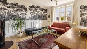 A living room with a red sofa, a glass coffee table, a potted plant, and a wall mural. - Apartment 'Erdgeschoss, 65qm' with Wi-Fi (Attendorn)