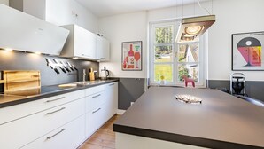 Een moderne keuken met witte kasten, een groot eiland en uitzicht op de omgeving door een raam.
