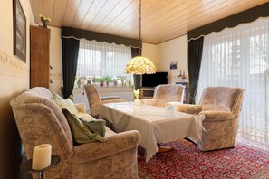 Un salon meublé comprenant une table, des chaises, un téléviseur et une lampe décorative.