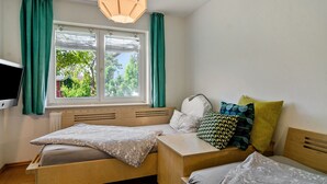 A room with two wooden beds, a window with curtains, a radiator, and a television on the wall.