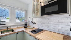 A modern kitchen with a built-in oven, a countertop with a kettle, and a window with a view of greenery. - Apartment 'Andrea' with Balcony and Wi-Fi (Langenargen)