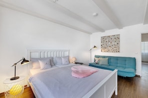A bedroom with a bed, bedside lamps, a sofa, and a wall art piece.