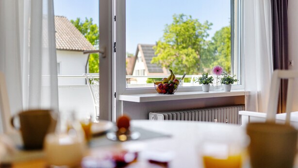A room with a window overlooking a residential area, a radiator below the window, and a table with various items. - Apartment 'Andrea' with Balcony and Wi-Fi (Langenargen)
