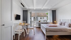 A bedroom with a bed, a desk with a chair, a television, and a view of a building through a window. - Apartment 'Andrea' with Balcony and Wi-Fi (Langenargen)
