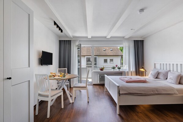 A bedroom with a bed, a desk with a chair, a television, and a view of a building through a window.