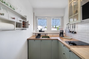A kitchen with a window, white cabinets, a black induction cooktop, and a coffee maker.