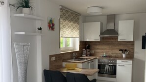 Une cuisine moderne avec des meubles blancs, un plan de travail en bois, un évier, un four et un coin repas avec deux chaises.
