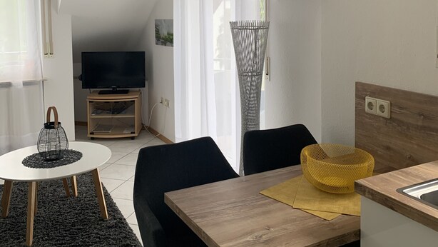 Un espace de vie moderne comprenant une table à manger, des chaises, un téléviseur et un coin cuisine.