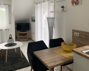 A modern living space with a dining table, chairs, a TV, and a kitchen area. - Big Apartment with Lake View, Balcony and Wi-Fi (Bodman-Ludwigshafen)