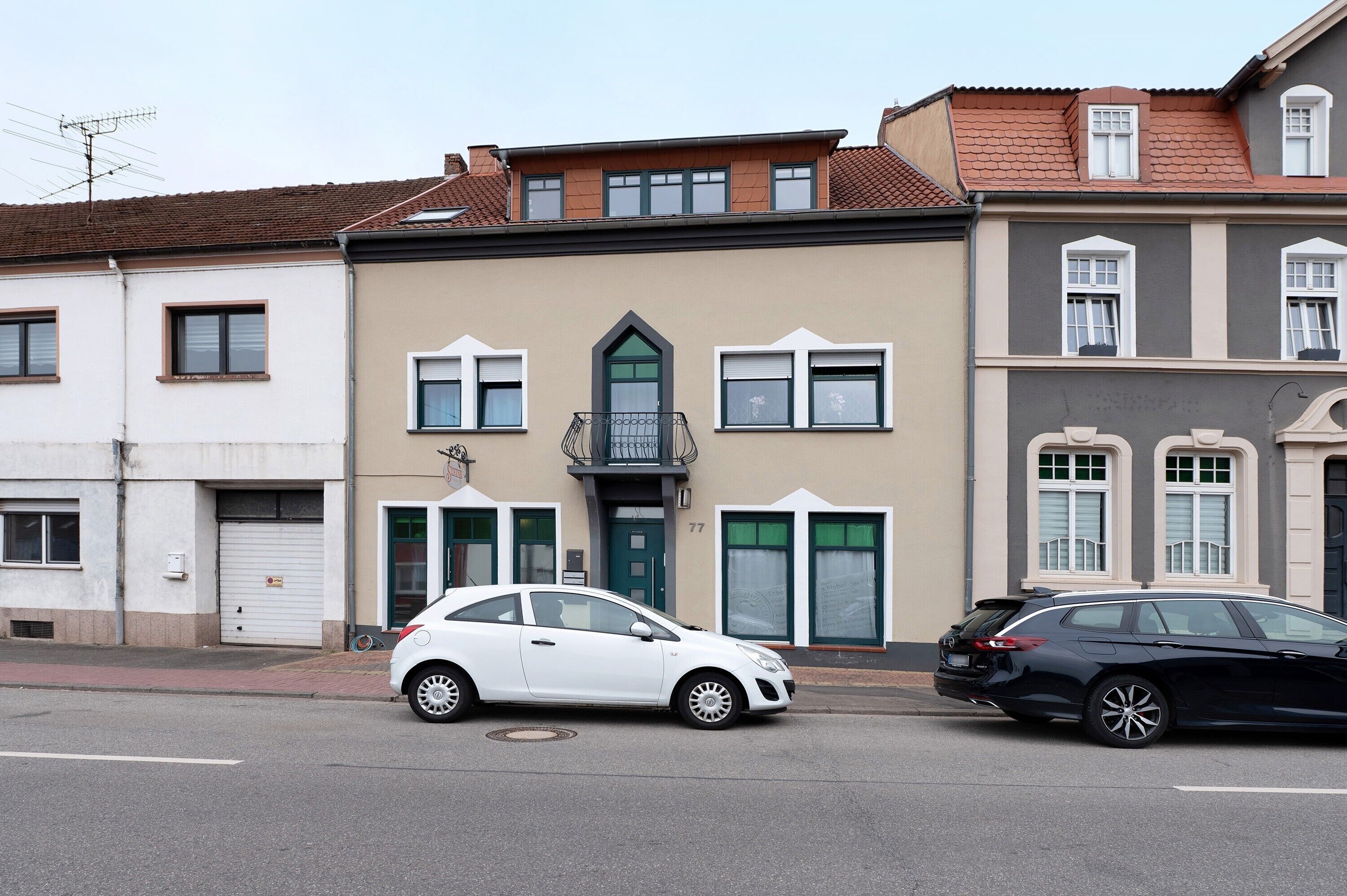 Une vue de rue avec deux voitures garées, un immeuble avec une porte verte et une fenêtre dotée d’un cadre blanc.