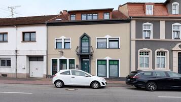 Une vue de rue avec deux voitures garées, un immeuble avec une porte verte et une fenêtre dotée d’un cadre blanc.
